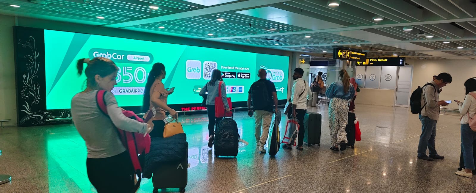 Iklan di Bandara Bali dari Grab menyambut penumpang yang tiba dengan promosi layanan transportasi, terlihat mencolok di koridor utama kedatangan.