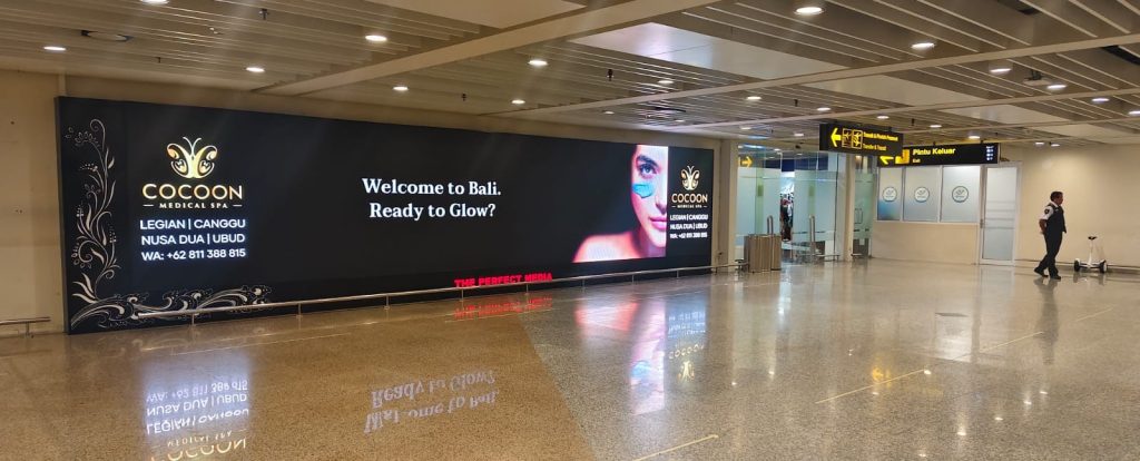 Iklan kesehatan Cocoon Medical Spa di layar LED Bandara Internasional I Gusti Ngurah Rai Bali dengan tagline Welcome to Bali Ready to Glow.
